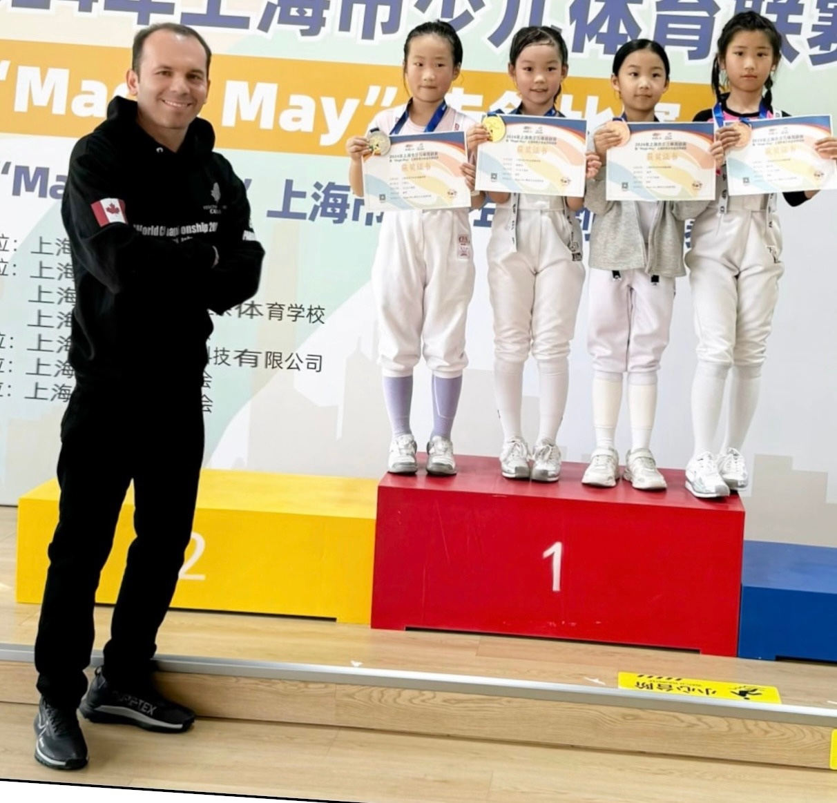 Coach Yousef Alaghehband with young fencing champions on a podium